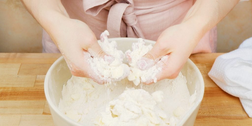 a baker's hands cutting butter into a bowl of flour