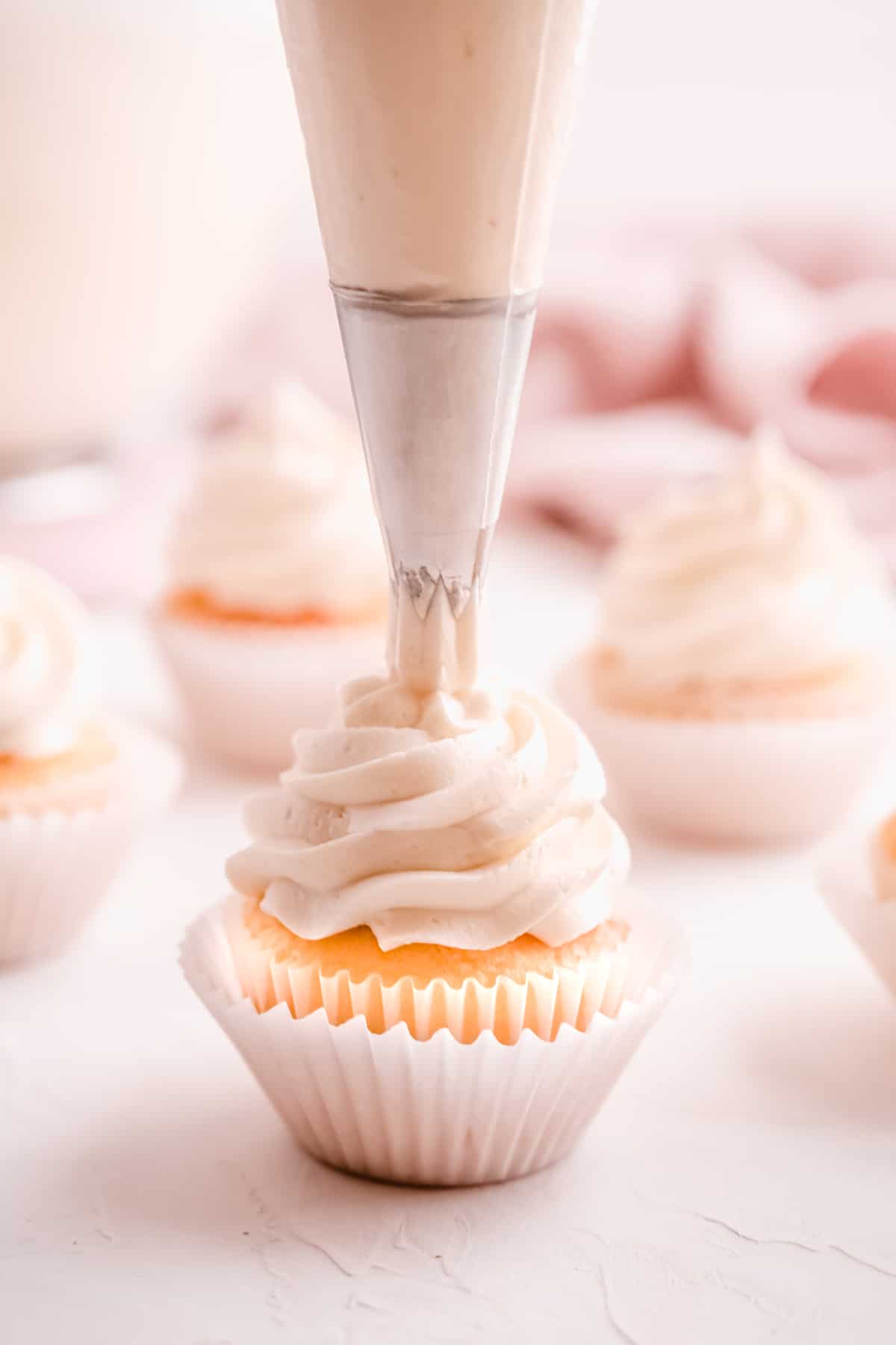 easy vanilla buttercream frosting being swirled on cupcakes from a pastry bag fitted with a star tip with other frosted cupcakes in the background