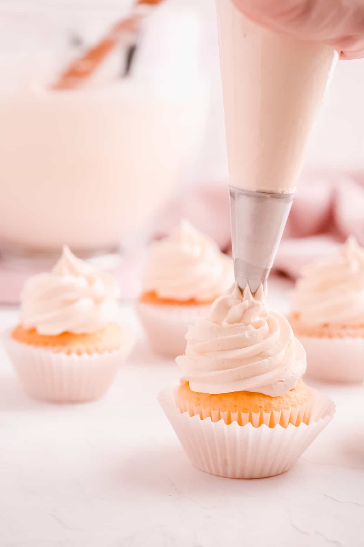 easy vanilla buttercream frosting being swirled on cupcakes from a pastry bag fitted with a star pip with other frosted cupcakes in the backgrounding tip