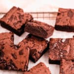 cut squares of fudgy gluten free brownies scattered on a wire cooling rack with parchment