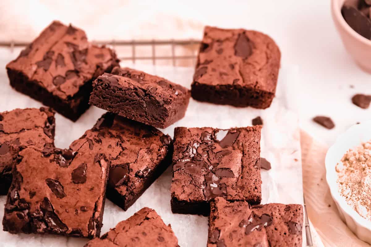 cut squares of fudgy gluten free brownies scattered on a wire cooling rack with parchment