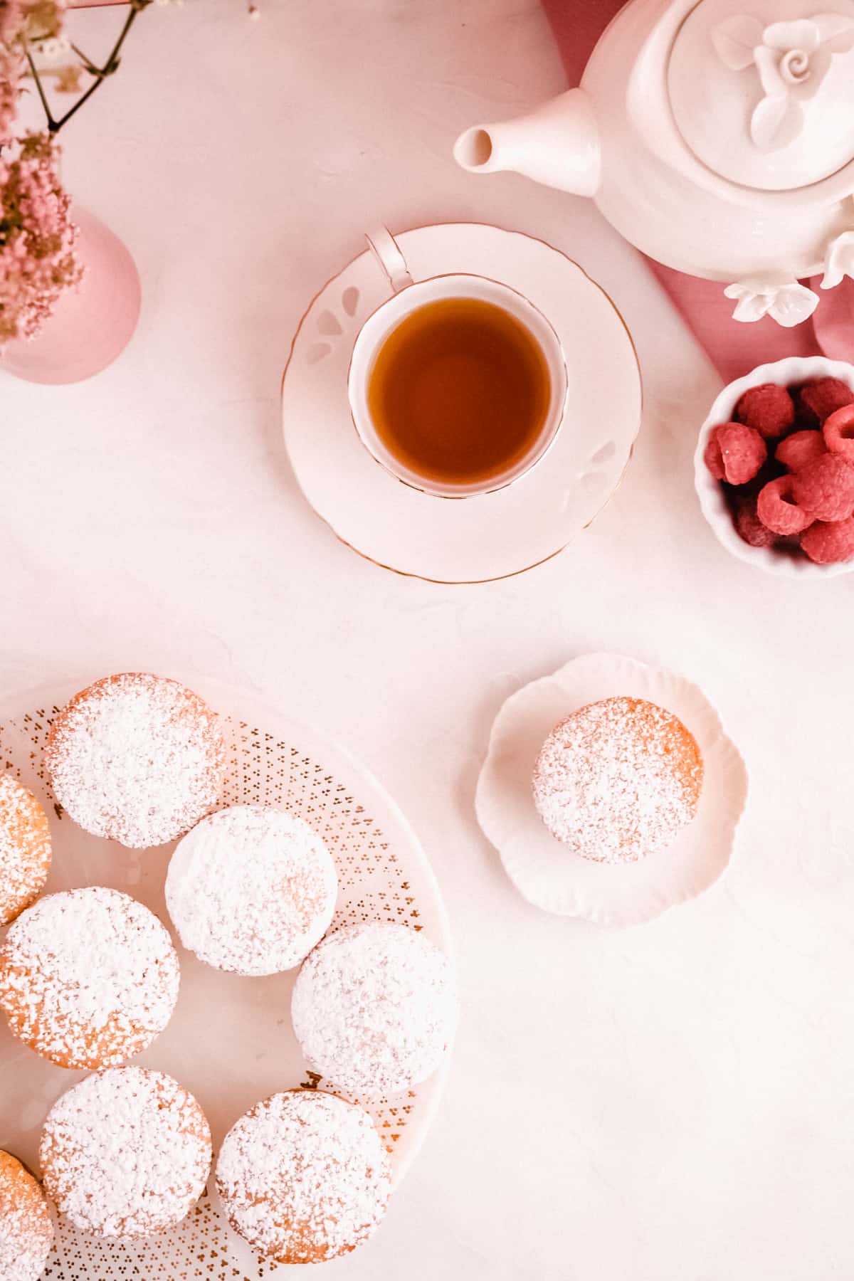 mini victoria sponge cakes filled with jam from above on a cake plate with raspberries, a cup of tea and a teapot