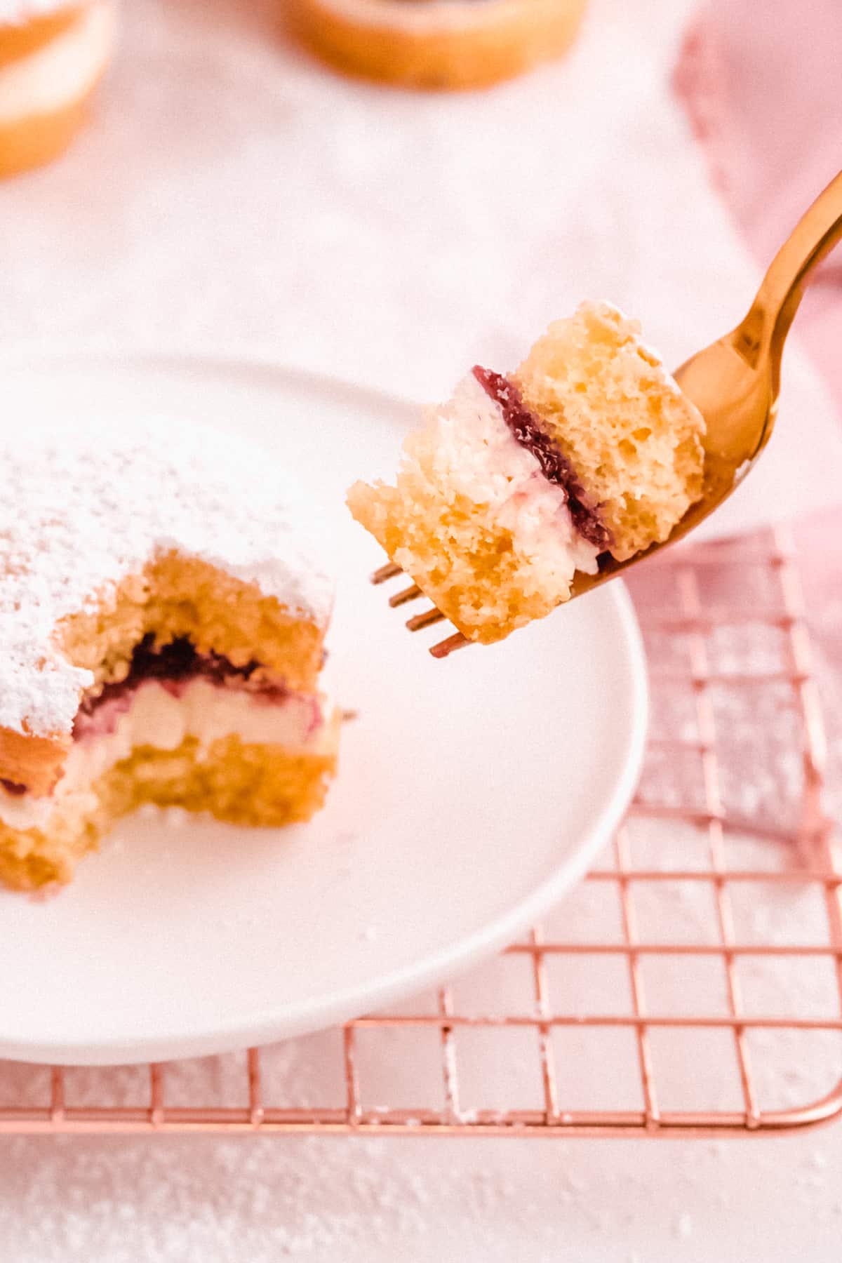 mini victoria sponge cakes filled with jam on a wire cooling rack with a bite taken out on a fork