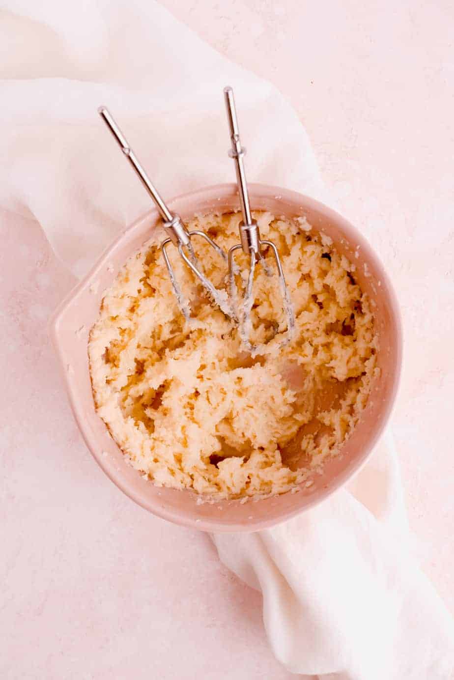 butter and sugar creamed in a bowl with pink background and silver beaters