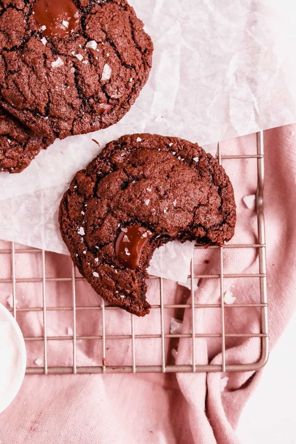 close up of a dark chocolate chip cookie on a wire tray with a bite out of it.