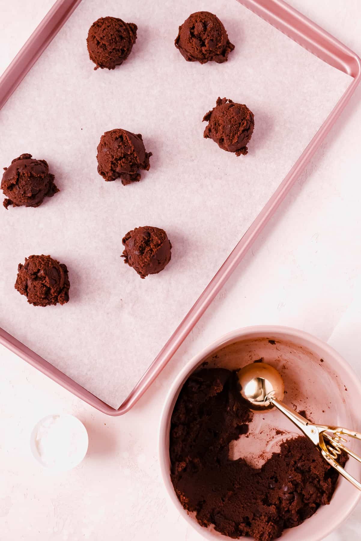 double chocolate chip cookie dough balls scooped and placed on parchment lined pink baking tray.