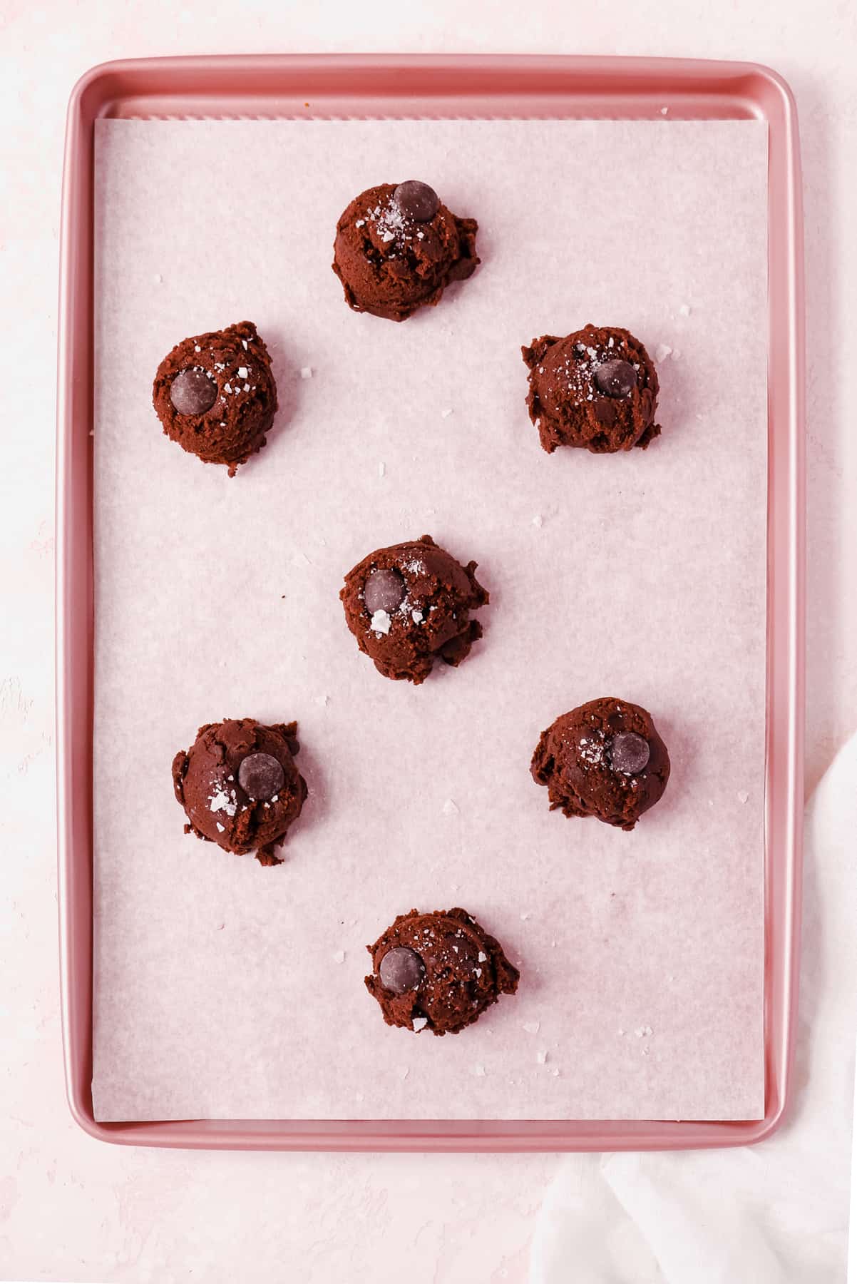 dark chocolate chip cookie dough balls spaced on a baking tray topped with sea salt.