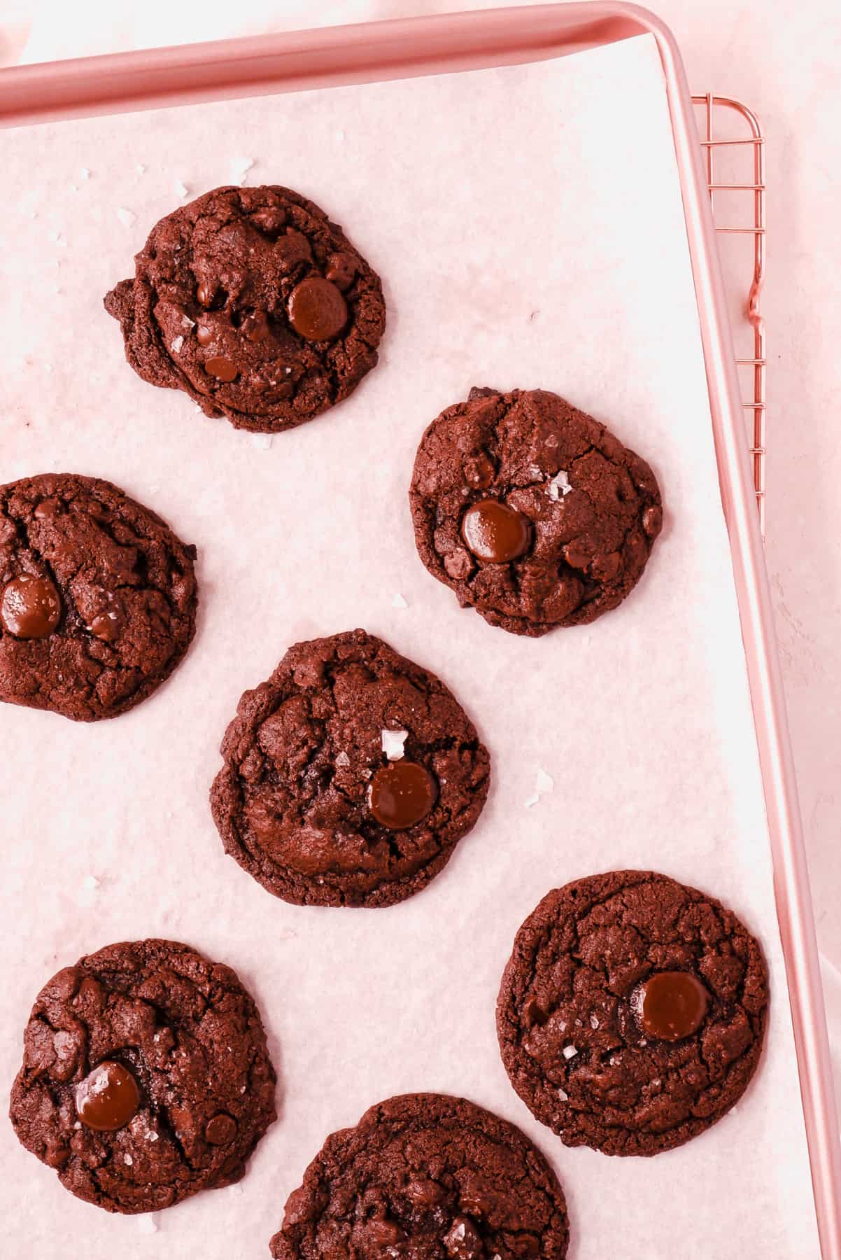 freshly baked dark chocolate chip cookies on a parchment lined pink baking tray.