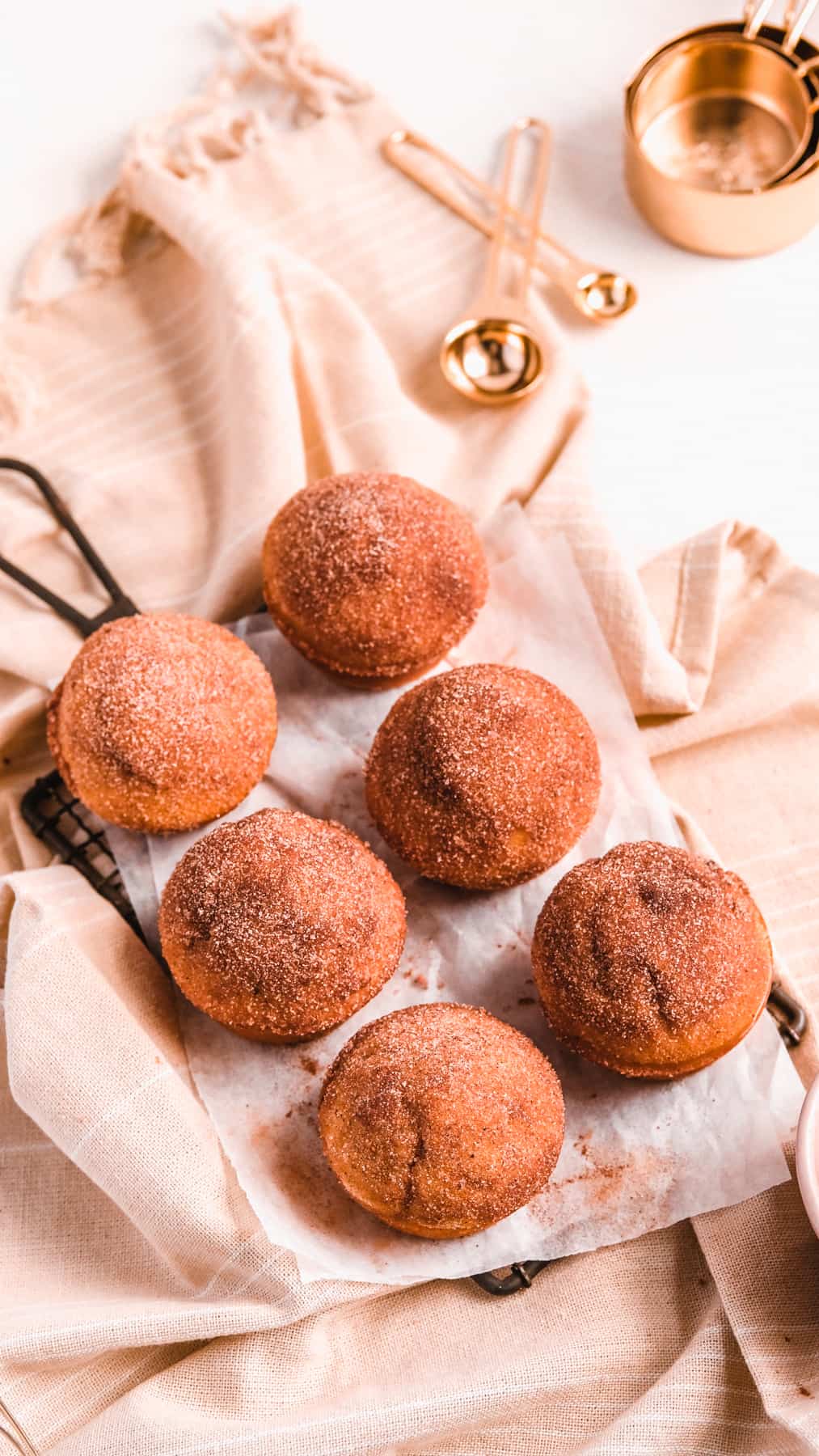 Cinnamon Donut Muffins on a wire rack with baking utensils around them