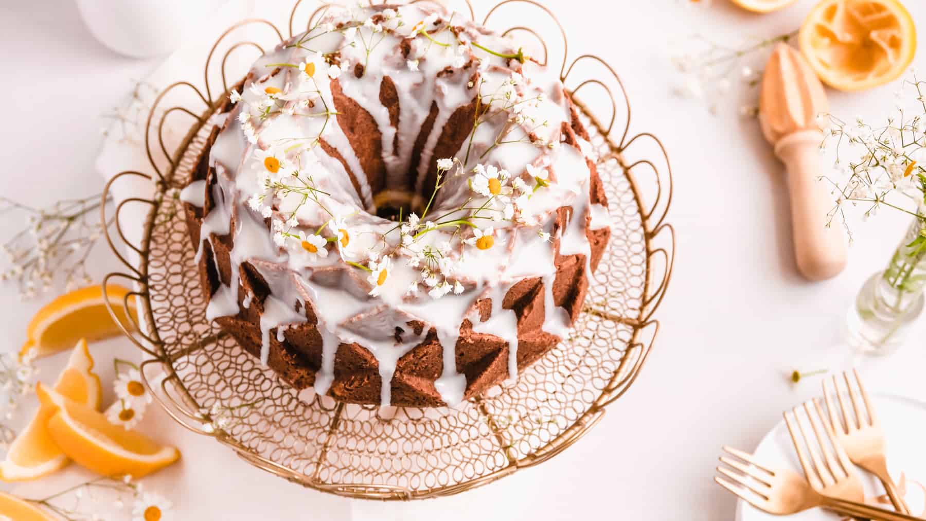 lemon bundt cake with lemon glaze and fresh flowers on a gold cake plate