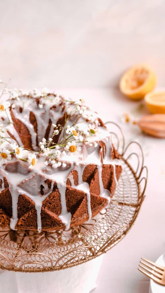 lemon bundt cake with lemon glaze and fresh flowers on a gold cake plate