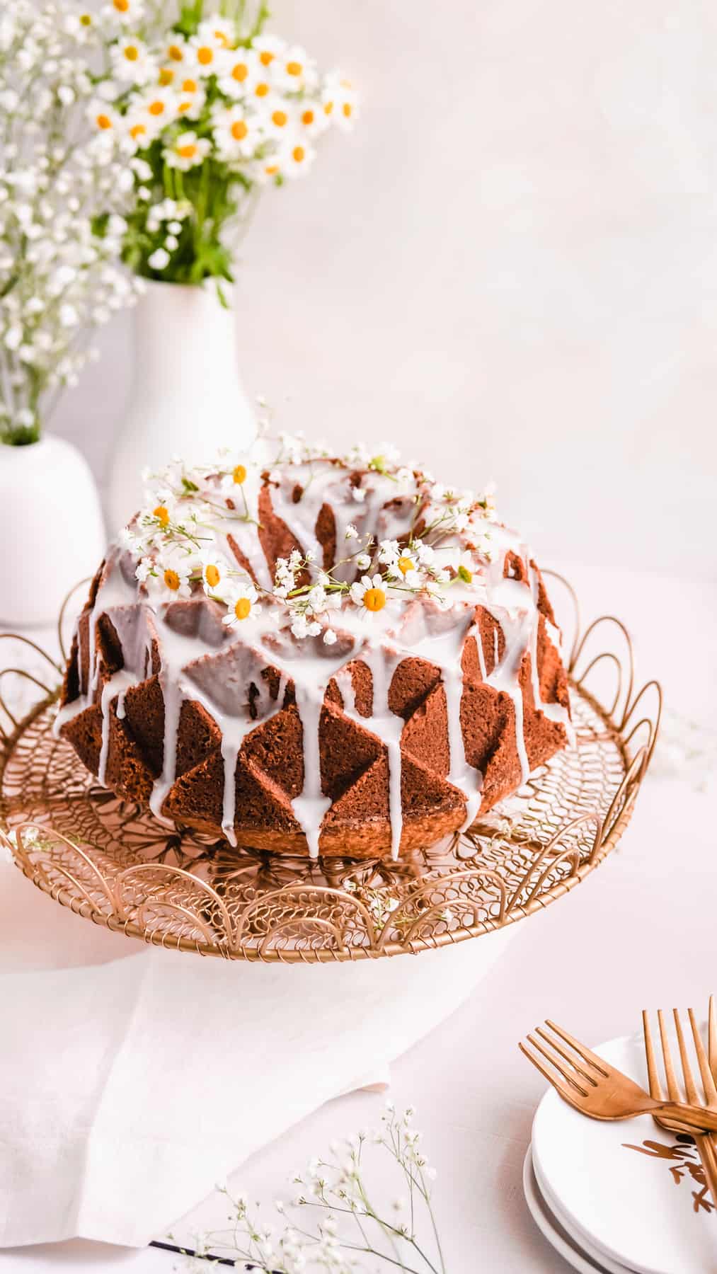 lemon bundt cake with lemon glaze and fresh flowers on a gold cake plate