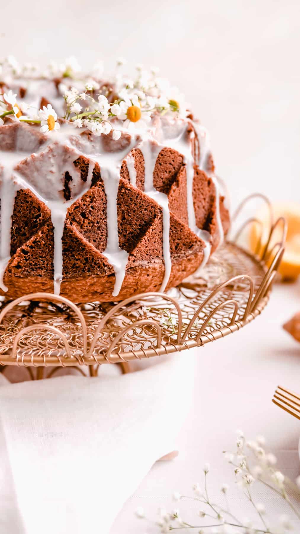 lemon bundt cake with lemon glaze and fresh flowers on a gold cake plate with lemons