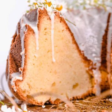 a cut lemon bundt cake with lemon glaze and fresh flowers on gold cake plate.