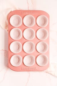 a pink muffin pan lined with white paper cups