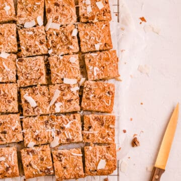 coconut butterscotch cookie bars on a wire rack with gold and wood knife.