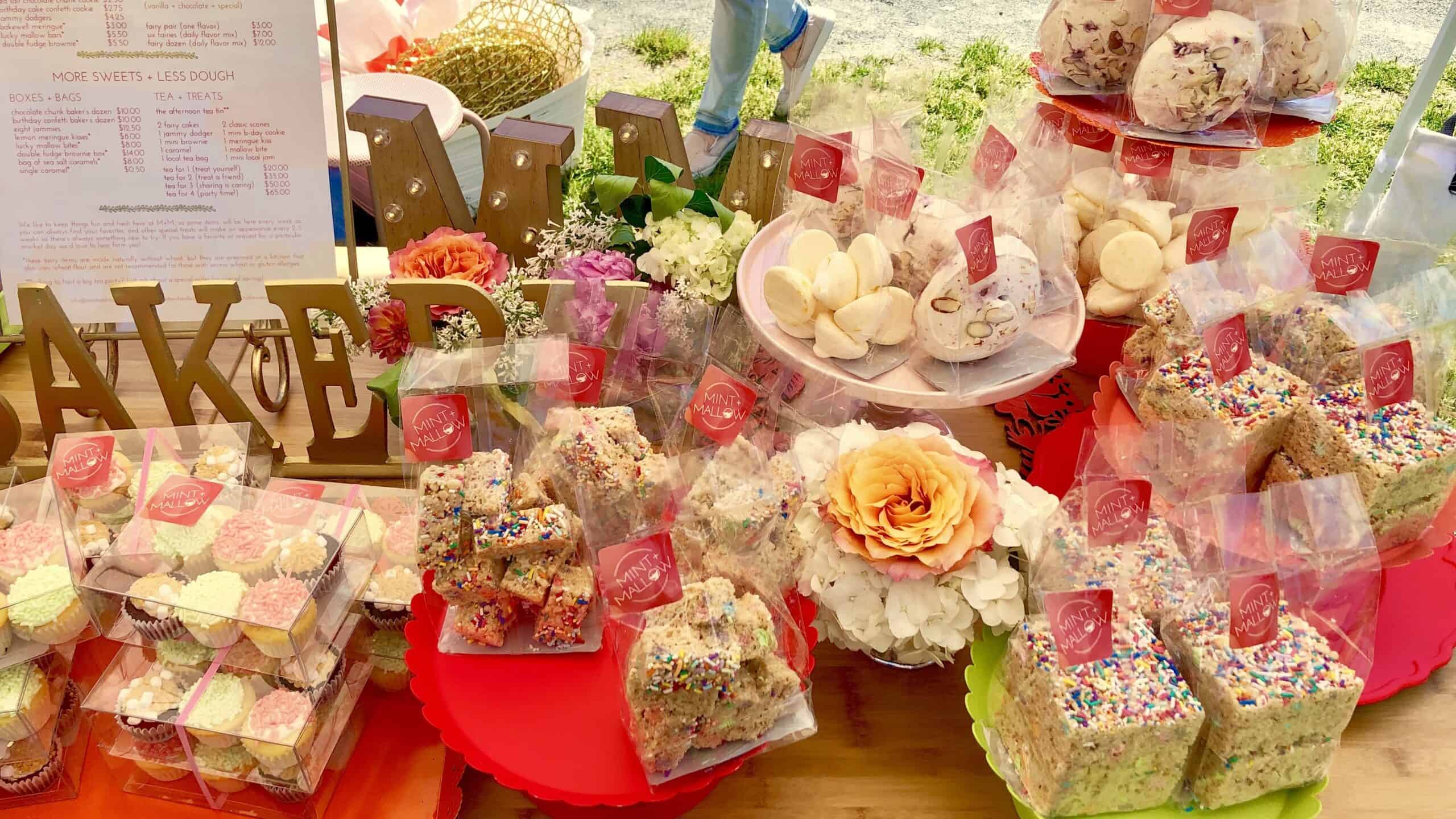 bags of meringues, cupcakes, and rice krispies on a table with pink trays and flowers in the background