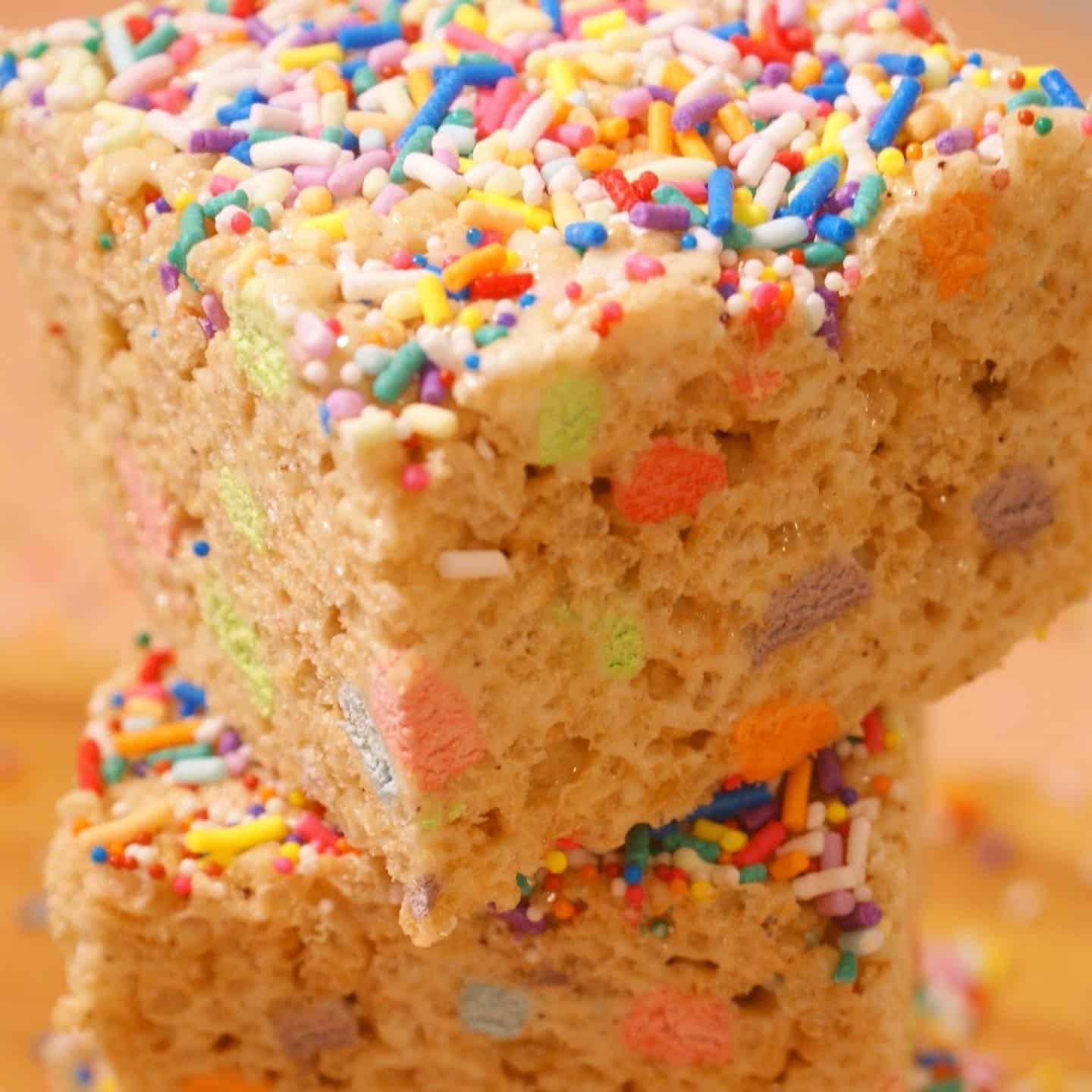 close up of rice krispie treats with rainbow sprinkles on top and rainbow marshmallow in them