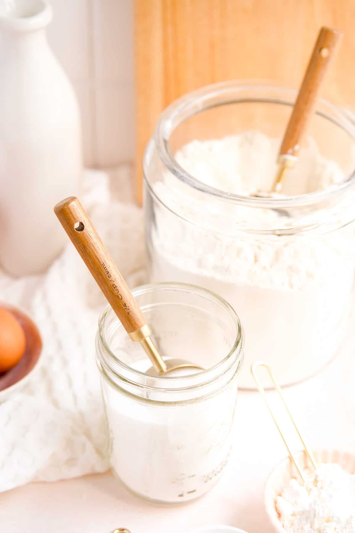 glass jars of flour and sugar with measuring cups in them.
