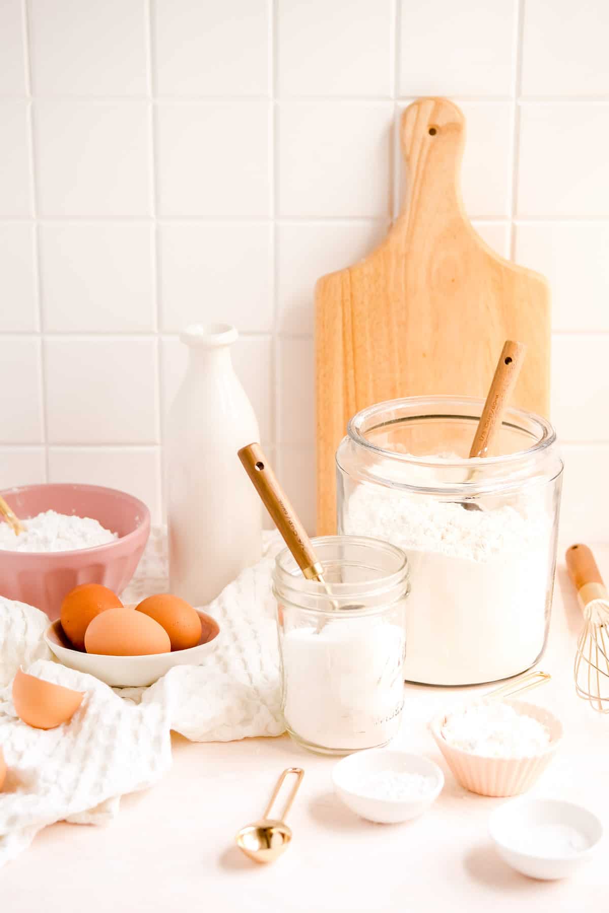glass jars and bowls of baking ingredients with measuring utensils.