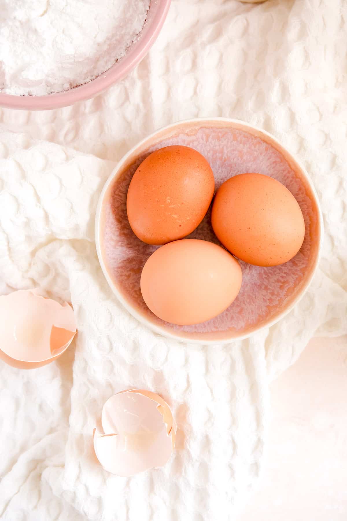 a bowl of 3 brown eggs with cracked egg shells on the side.