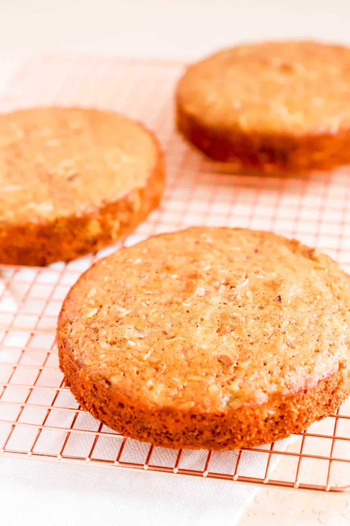 3 baked round carrot cake with pineapple layers on a copper cooling rack.