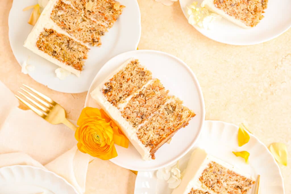 old-fashioned carrot cake slices on plates stacked up with ranunculus flowers for decoration.