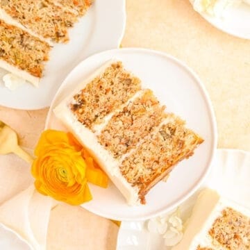 carrot cake with pineapple slices on plates stacked up with ranunculus flowers for decoration.