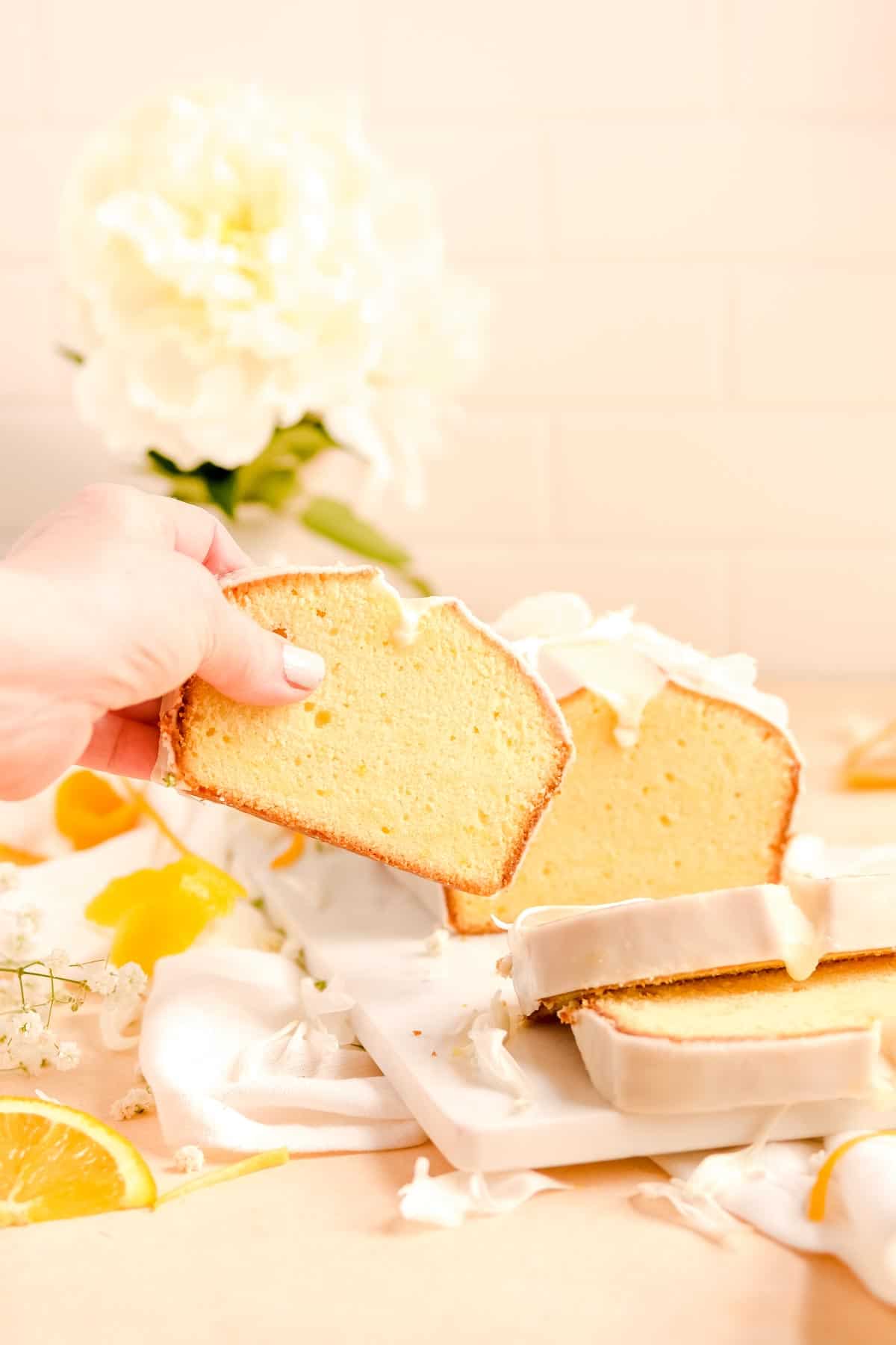 someone grabbing a slice of glazed citrus pound cake from a a table with flowers and orange slices on it.