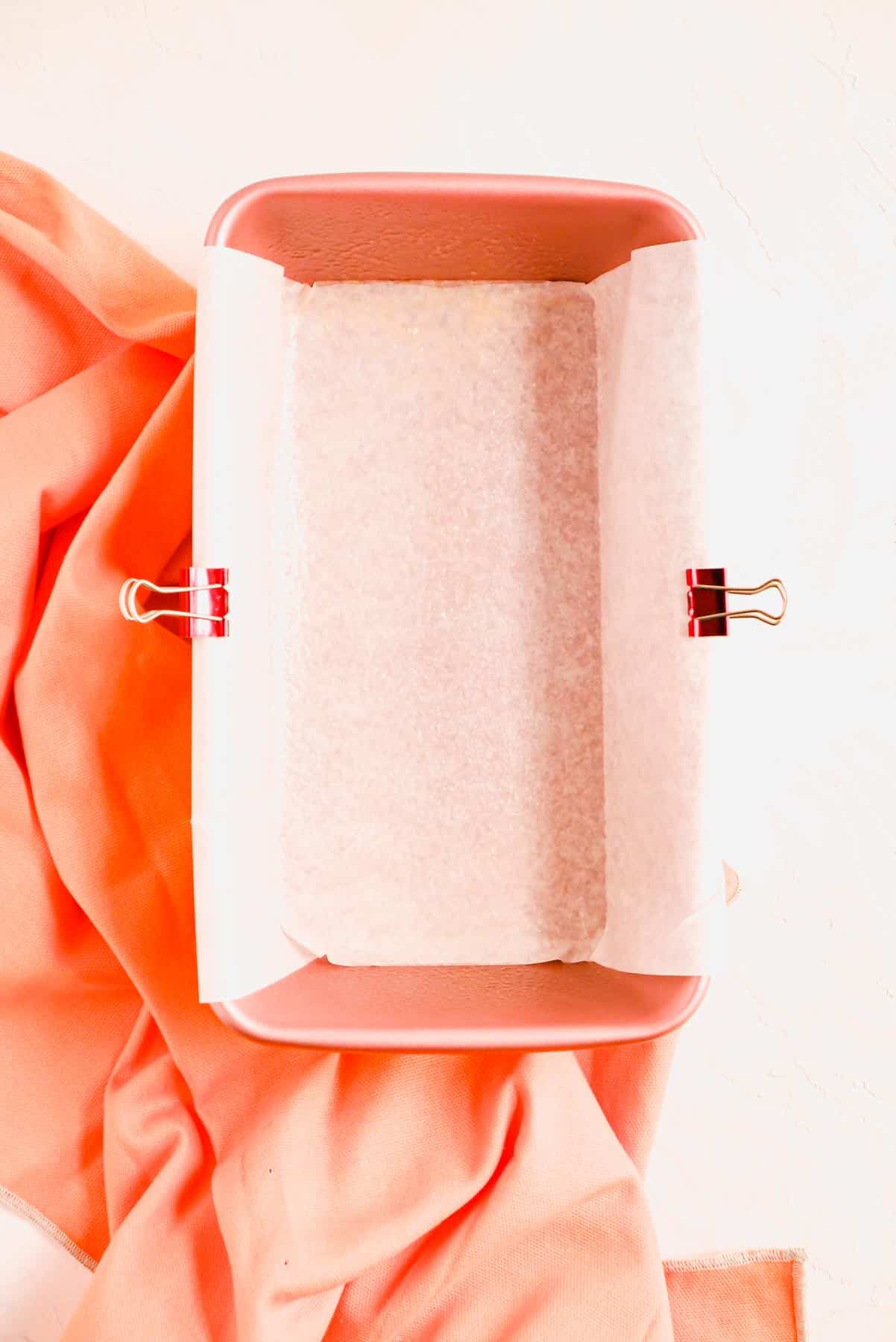 a parchment-lined pink loaf pan on a pink towel.