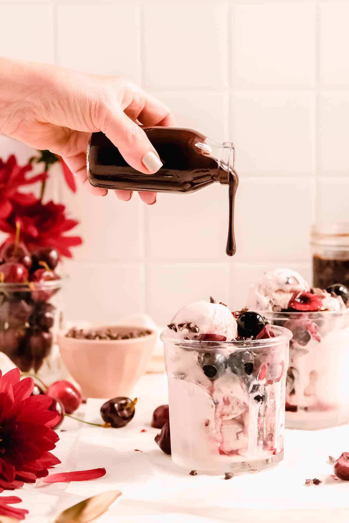 homemade hot fudge mid-pour from a bottle onto a cherry ice cream sundae.