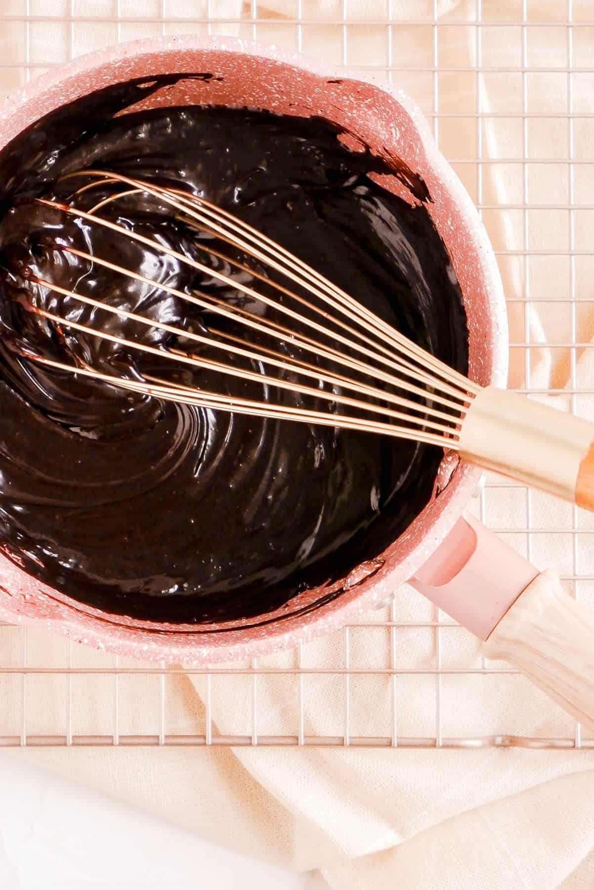 all the hot fudge sauce ingredients in a pot with a gold whisk fully cooked and thickened.