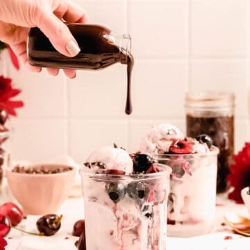 homemade hot fudge mid-pour from a bottle onto a cherry ice cream sundae.