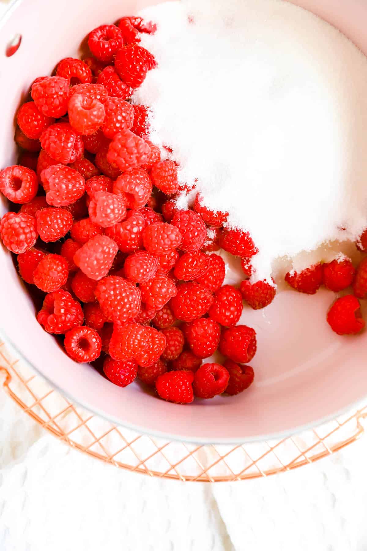 a pink pot on a cooling rack with raspberries, sugar, and lemon juice in it.