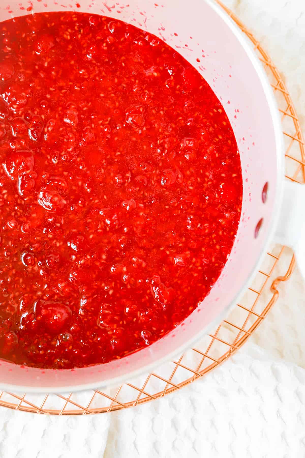 a pink pot on a cooling rack with a slurry of raspberries and sugar in it.