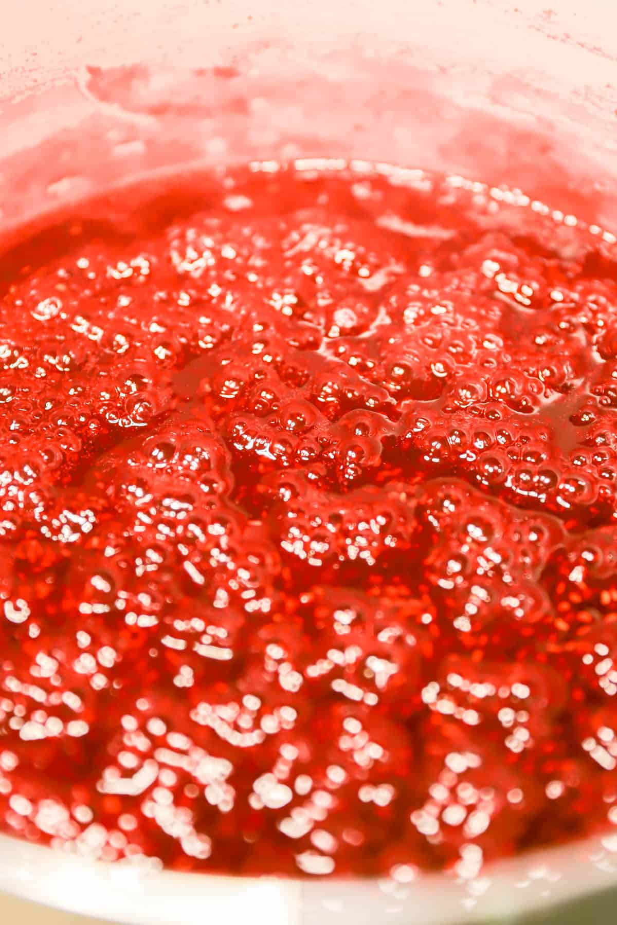 bubbling homemade french raspberry jam close up in a pink pot.