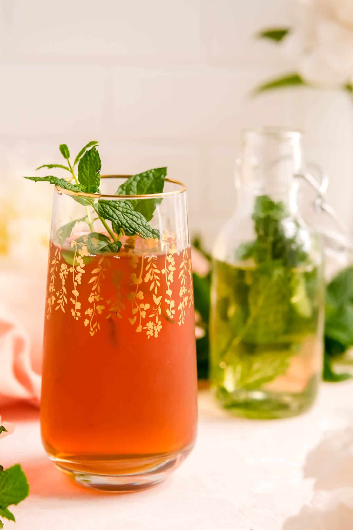 a glass of iced tea with a partial bottle of mint syrup in the background.