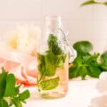 a partial bottle of mint simple syrup with a mint leaf in it.