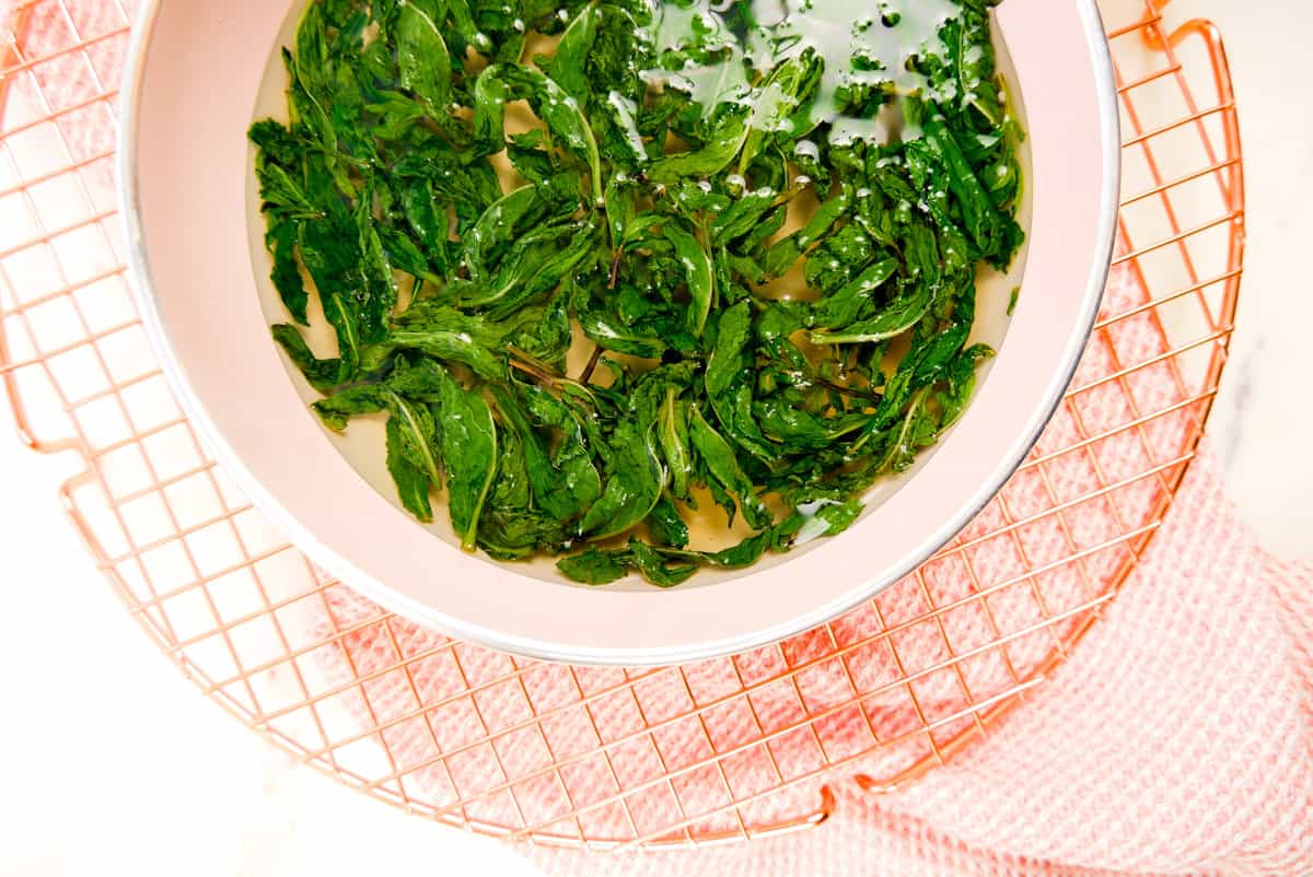 mint leaves just added to a pan of hot simple syrup on a wire rack set on a pink towel.