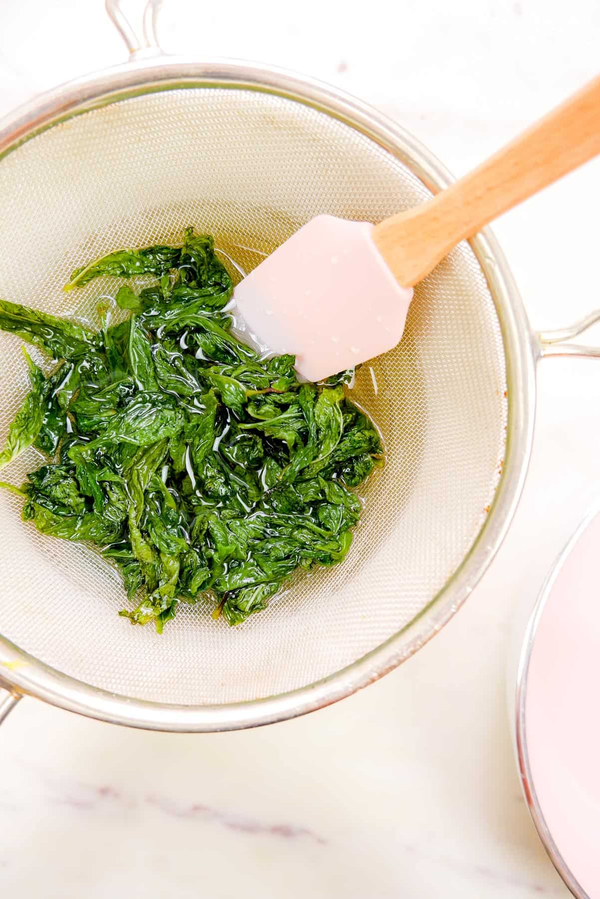 mint leaves being strained our of the simple syrup over a bowl.