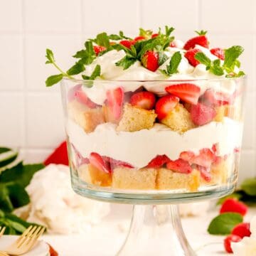 a strawberry trifle from the side showing the layers with plates, forks and flowers on a table.