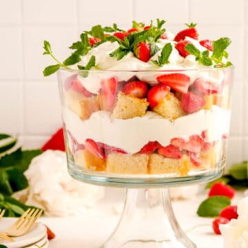 a strawberry trifle from the side showing the layers with plates, forks and flowers on a table