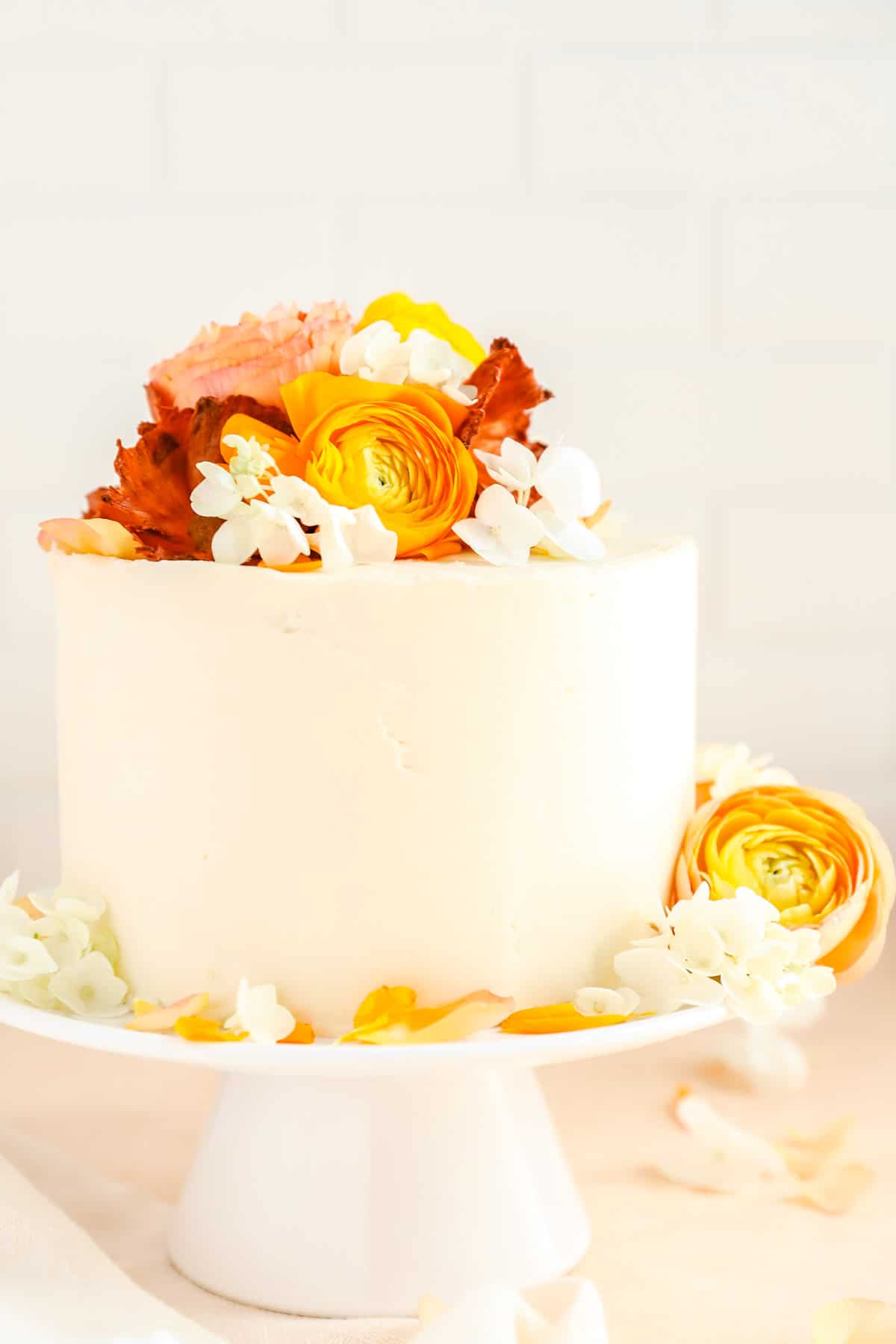 a cake covered in smooth white frosting with hydrangea and ranunculus flowers on top.