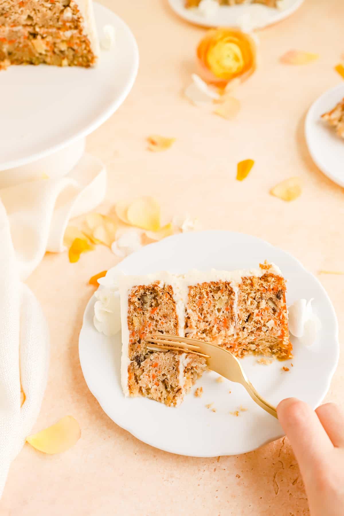 a hand using a fork to take a bite out of a piece of carrot cake.