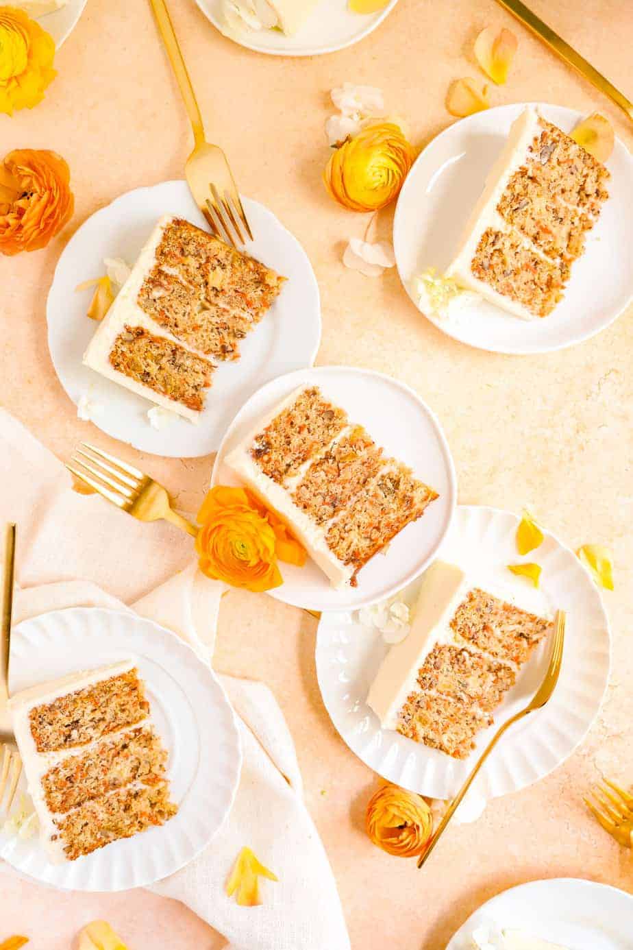 a bunch of carrot cake slices on plates with gold forks and flowers scattered around.