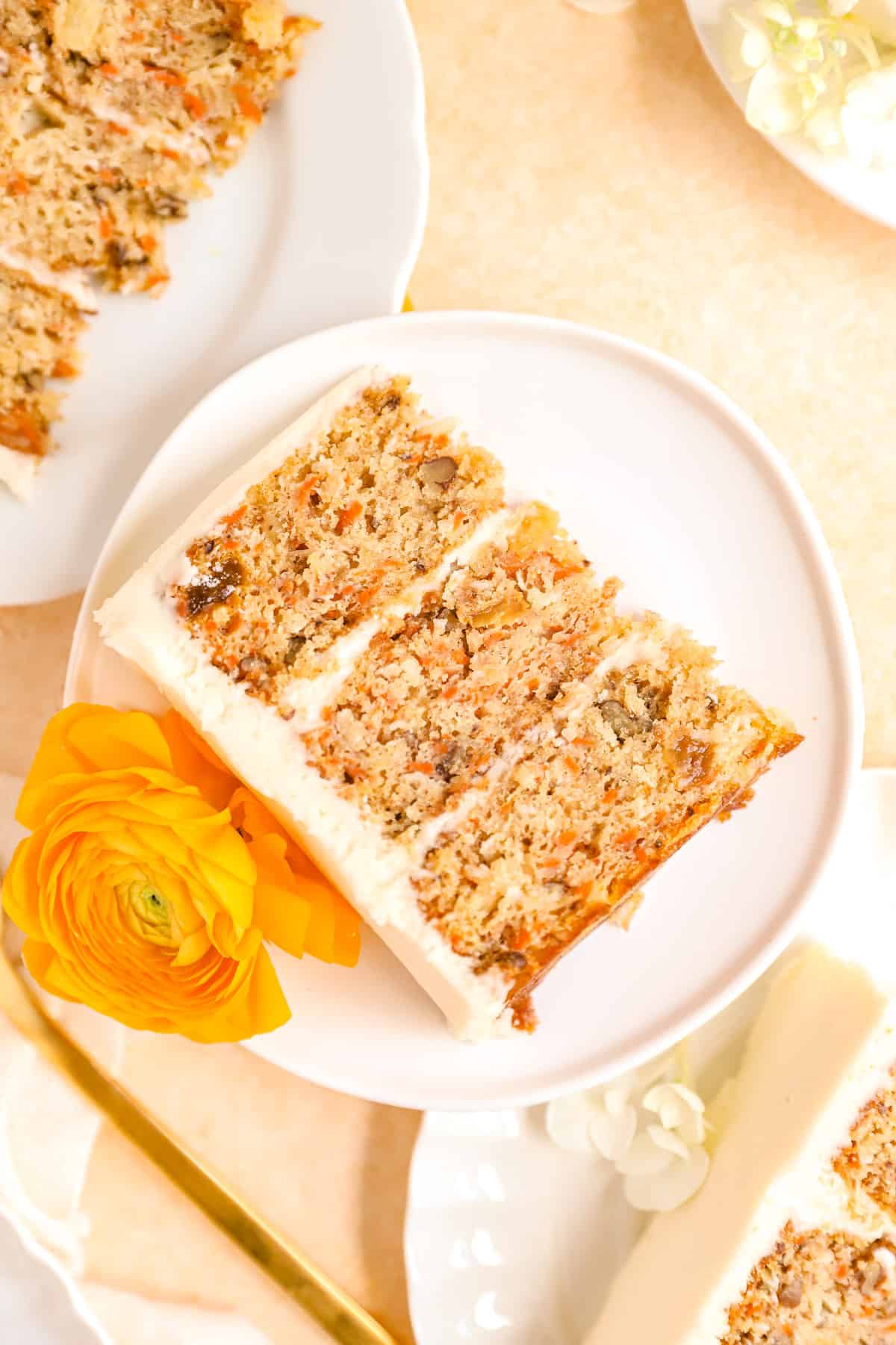 carrot cake with pineapple slices on plates stacked up with ranunculus flowers for decoration.