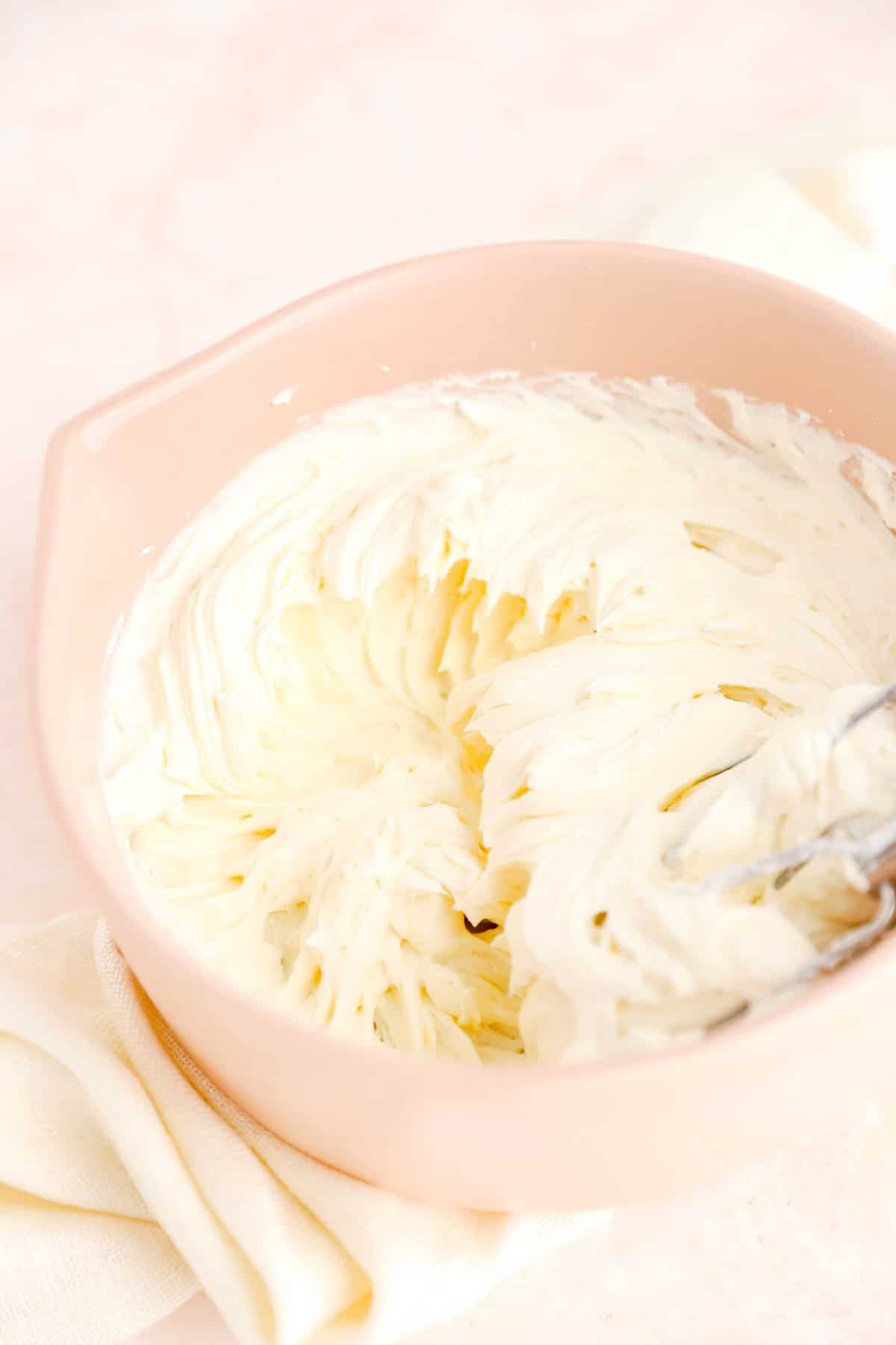 a tan bowl of whipped butter, cream cheese, and powdered sugar on a white linen.