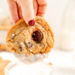 a close up of a chocolate chip cookie with a hand having just dunked it in milk