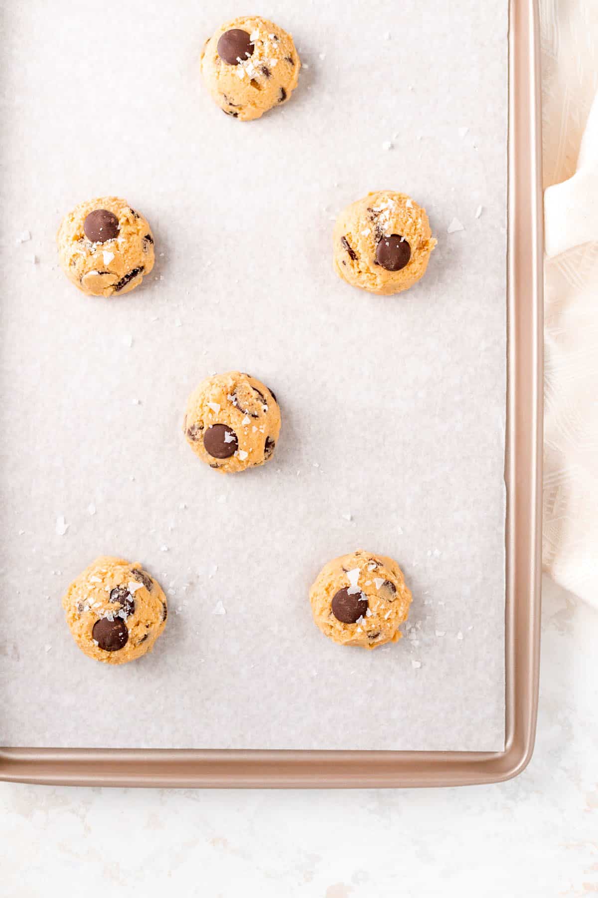 chocolate chip cookie dough balls with salt on a gold parchment baking sheet