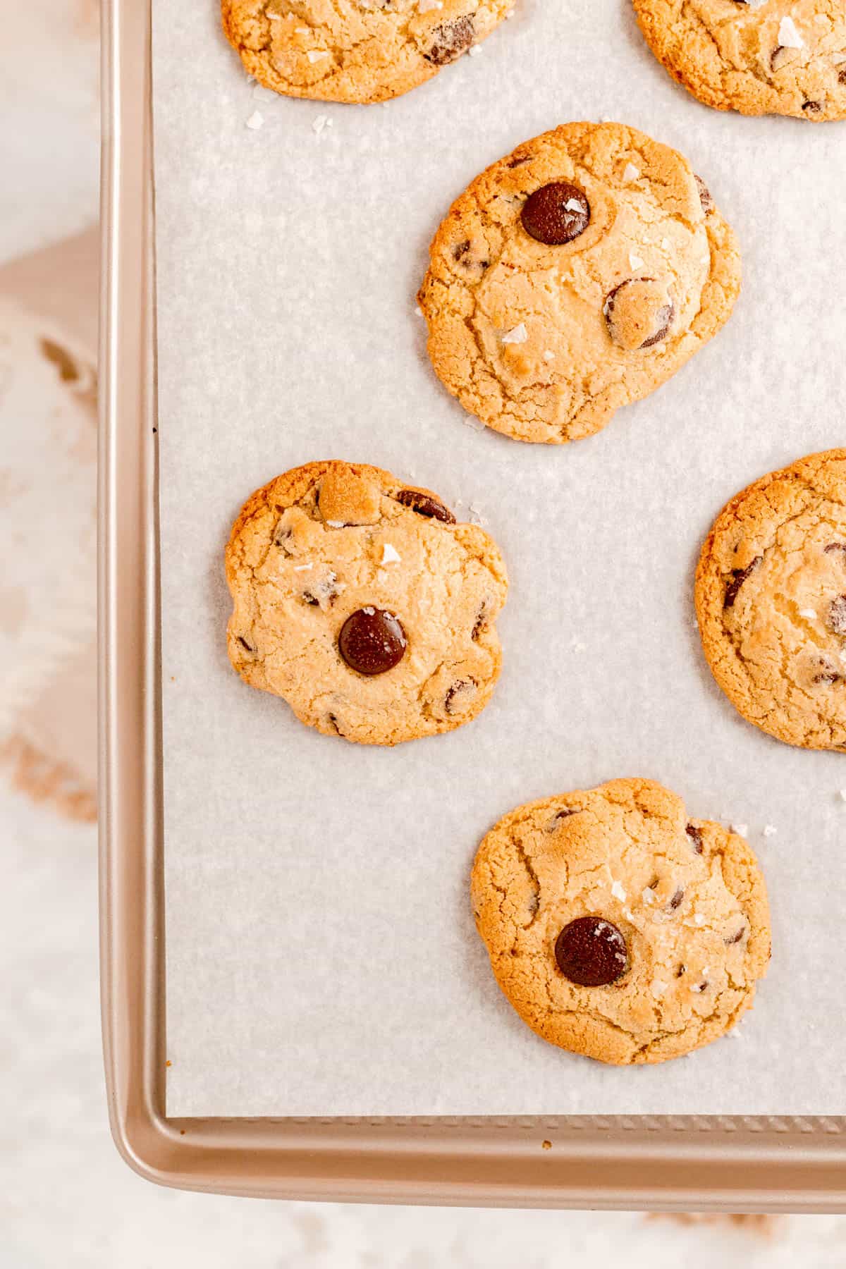 baked and puffy salted chocolate chip cookies on a gold cookie sheet.